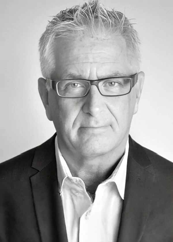 Professional headshot of a middle-aged man with gray hair and rectangular glasses, wearing a dark blazer and white shirt in black-and-white.