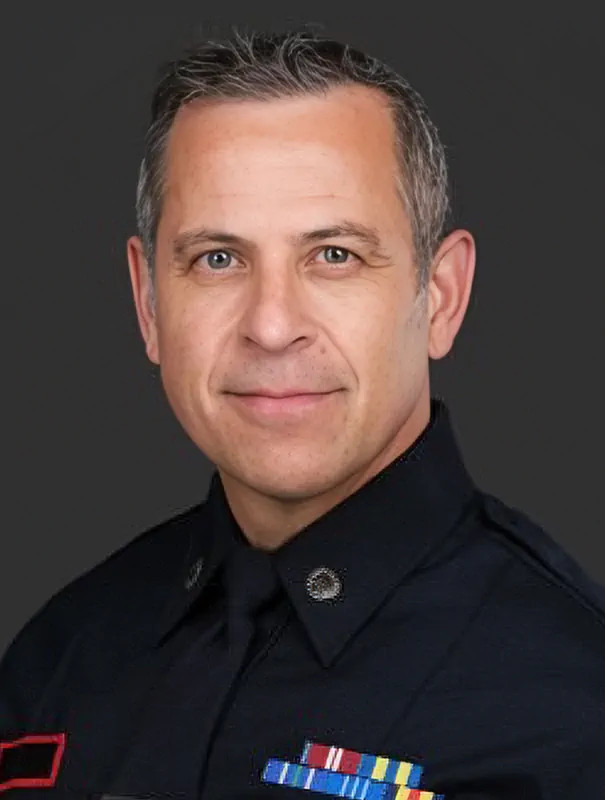 Portrait of a uniformed officer wearing a dark shirt with ribbons and medal pins visible on the chest.